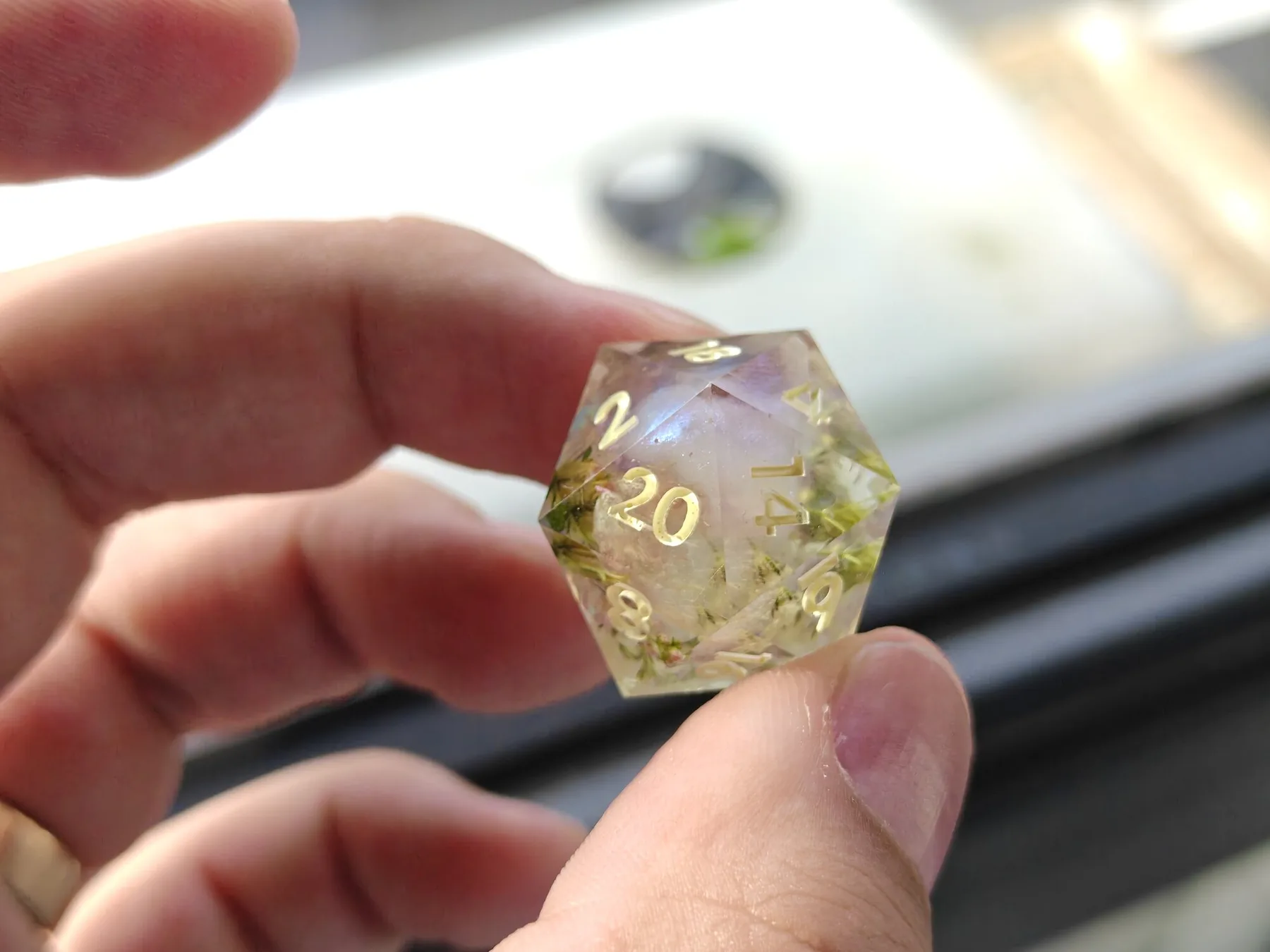 Een d20 van resin tussen duim en wijsvinger